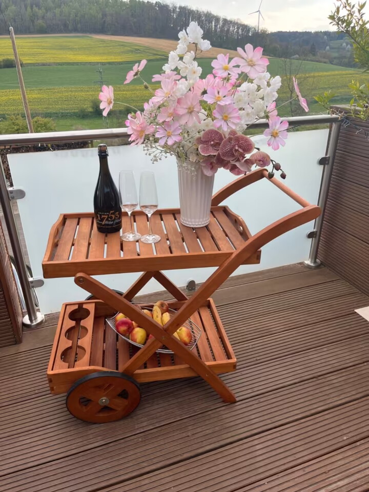 Servierwagen aus Holz, zwei Ablagen, mit Blumenstrauß, Flasche Sekt und Gläsern dekoriert, auf Balkon platziert